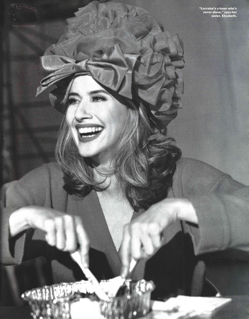 Editorial photo from Connoisseur magazine featuring actress Lorraine Bracco smiling. She is wearing a large, elaborate ruffled hat with a bow while using a knife and fork over a foil container.