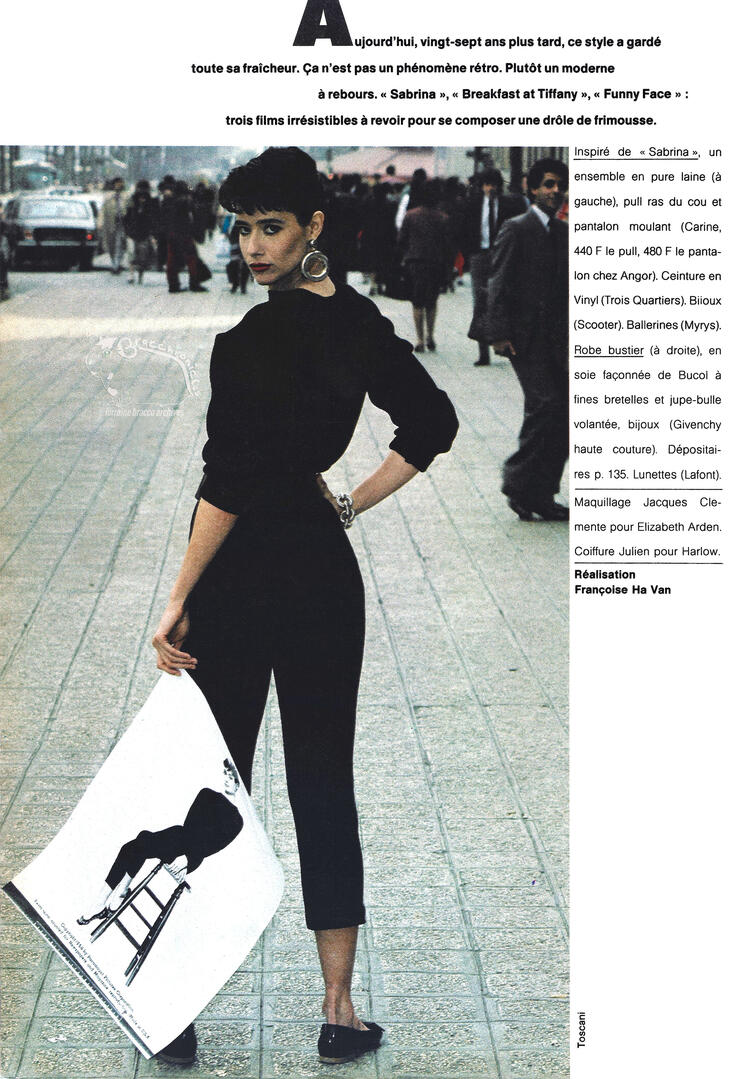 Continuation of Elle magazine page layout with French text featuring Lorraine Bracco standing on a city sidewalk in an all-black ensemble with cropped pants and flats. She faces away from the camera, holding a large print of Audrey Hepburn.