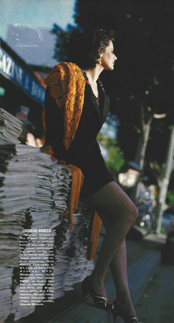 Self magazine fashion spread featuring Lorraine Bracco leaning against a large stack of newspapers on a city street, wearing a black dress and a bright orange shawl.