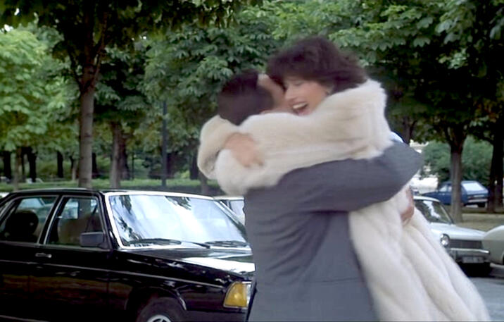 1 Actress Lorraine Bracco hugging a man outdoors next to a vintage car in a scene from the 1979 French comedy film Duos sur canapé.