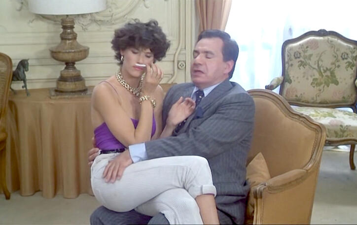 9 Lorraine Bracco sitting on a man's lap in a living room scene from the 1979 French comedy film Duos sur canapé.