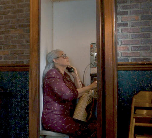 9 Lorraine Bracco talking on a vintage payphone inside a wooden booth in the Netflix film Nonnas.