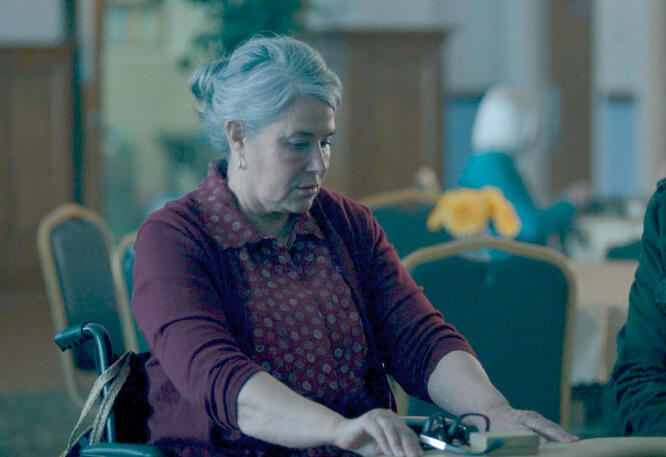 8 Lorraine Bracco in a maroon patterned shirt looking down at a table in a scene from Nonnas.
