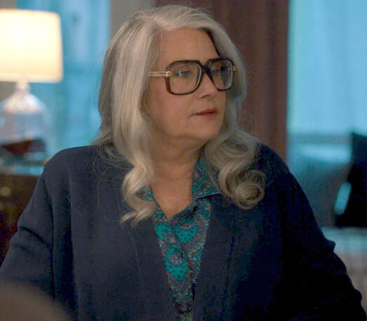 12 Lorraine Bracco with grey hair and giant glasses looking sideways in a scene from Nonnas film.