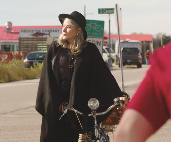11 Lorraine Bracco pushing a bicycle on an outdoor street in Monster Summer.