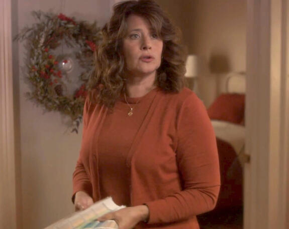 3 Lorraine Bracco in an orange top looking surprised in a scene from the festive movie Snowglobe.