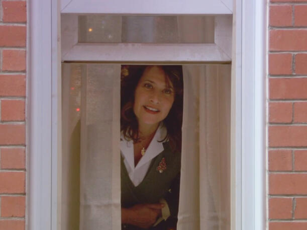 1 Lorraine Bracco peeking through a window curtain in a scene from the Christmas movie Snowglobe.