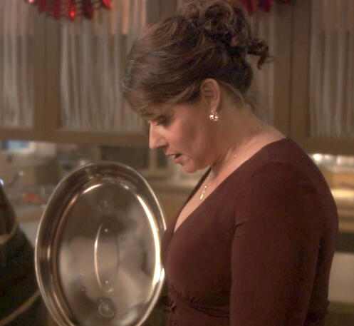 4 Lorraine Bracco looking down at the food she made while holding a metal pot lid in a dinner scene from Snowglobe.