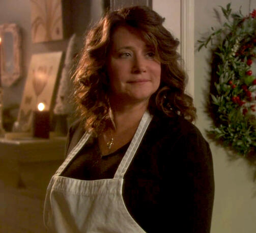 10 Lorraine Bracco wearing an apron and smiling next to a Christmas wreath in a scene from Snowglobe.