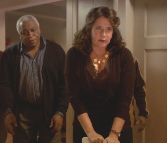12 Lorraine Bracco leaning against a chair next to her husband in a scene from the festive film Snowglobe.