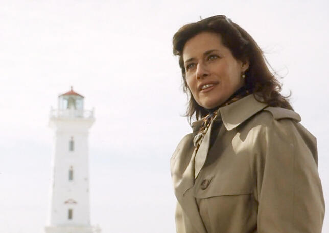 4 Actress Lorraine Bracco in a tan trench coat next to a white lighthouse in Custody of the Heart.