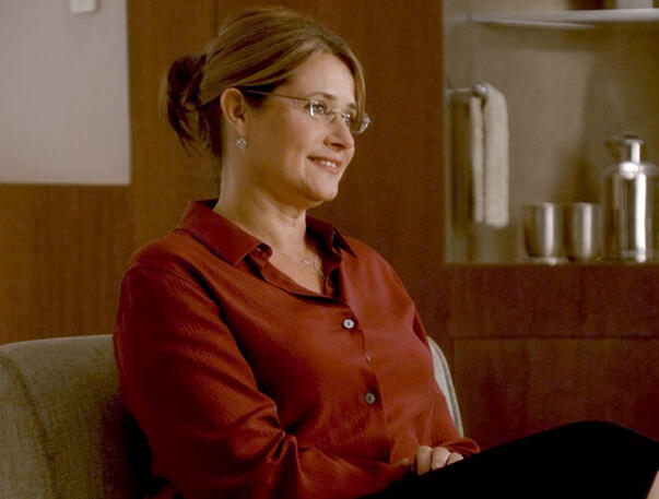 12 Dr. Melfi smiling warmly at Tony Soprano in a red button-down shirt and glasses during a scene in The Sopranos.