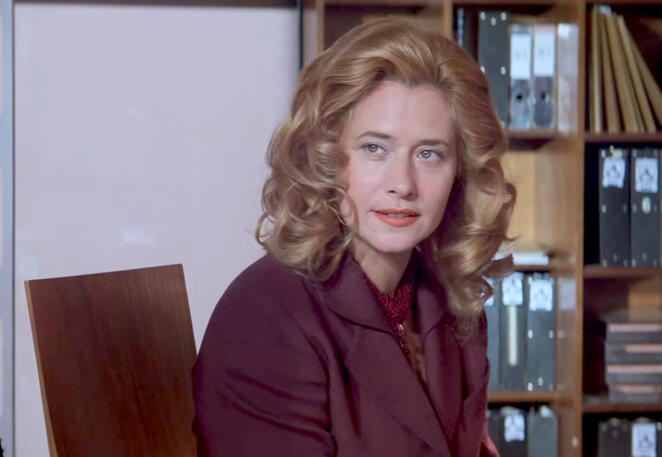 4 Lorraine Bracco sitting at a desk with binders behind her in a scene from Hackers.