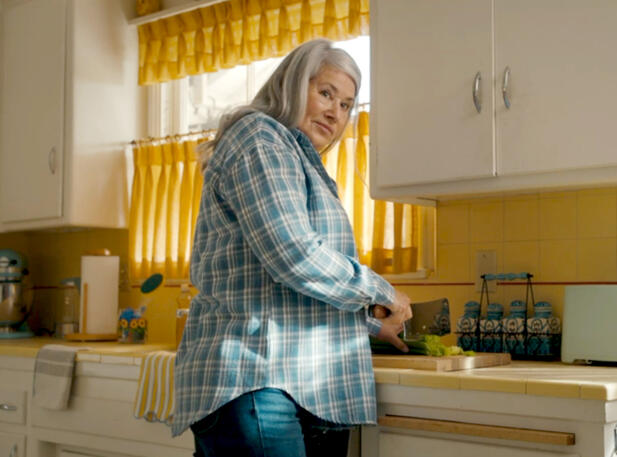 4 Lorraine Bracco in a plaid shirt chopping food in kitchen for The Mother, the Menacer, and Me.