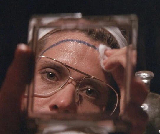 7 Lorraine Bracco looking in a mirror trying to wipe blue paint from her forehead in Medicine Man.