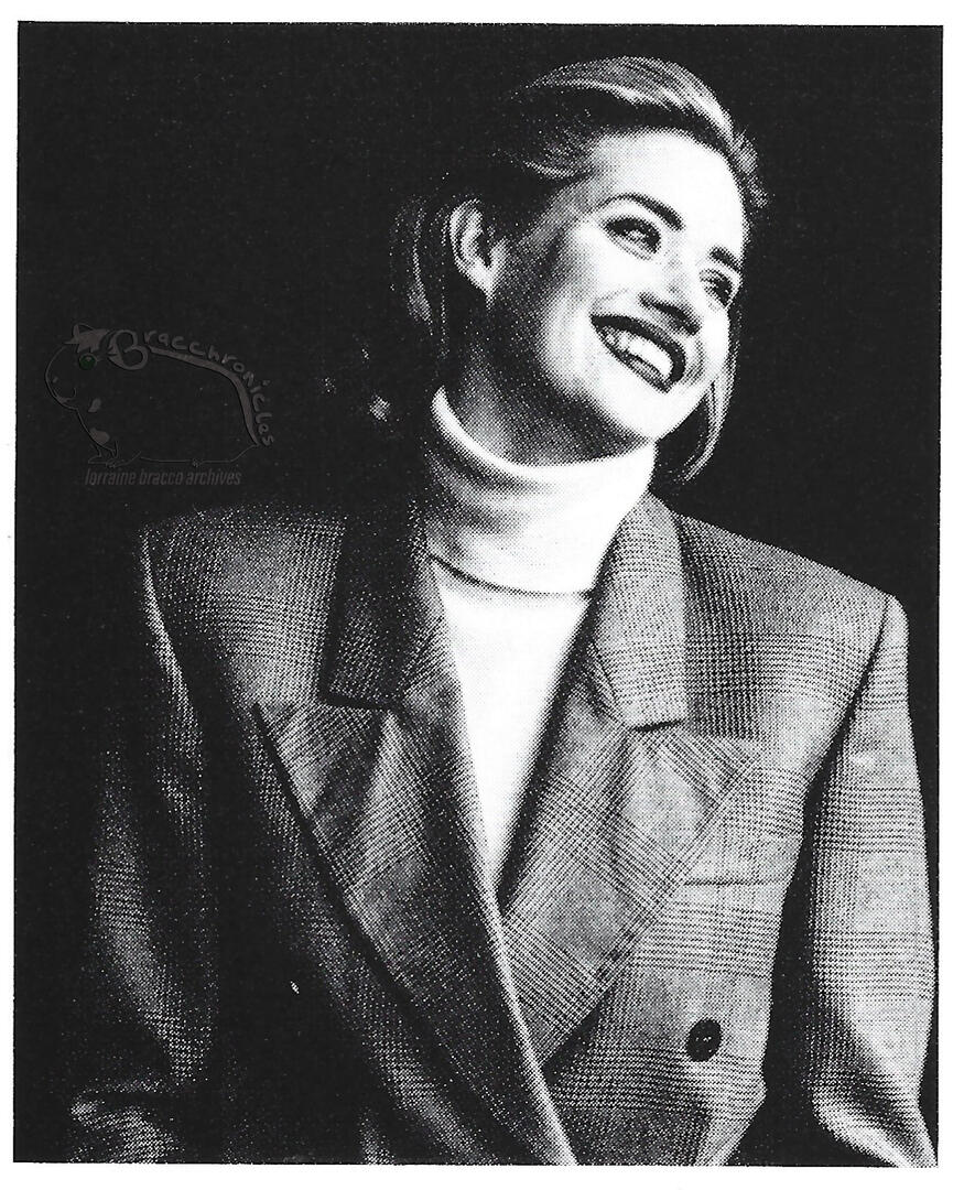 Mirabella magazine Table of Contents extra featuring black and white fashion portrait of a smiling actress Lorraine Bracco against a dark background in a plaid Gucci suit.